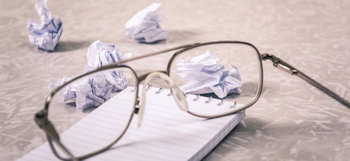 Glasses on top of notepad with wadded up papers