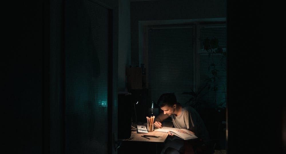 Person sitting at a desk writing in the light of a lamp